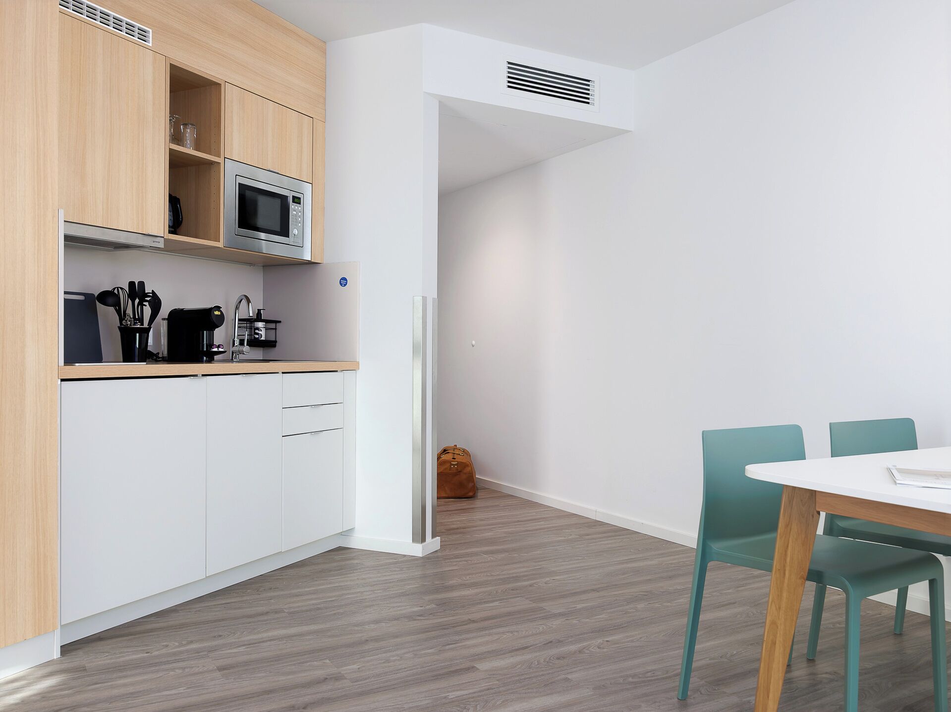 A modern kitchen with white cabinets, a microwave, and a coffee maker. There is a dining area with a table and chairs.