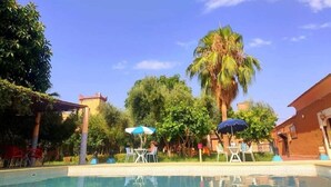 Ein Swimmingpool mit Liegestühlen und Sonnenschirmen, umgeben von viel Grün und blauem Himmel.