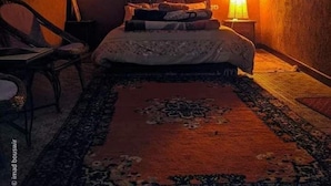 Ein Schlafzimmer mit Bett, Nachttisch, Sessel, Teppich und einer Wandlampe.