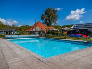 A swimming pool with lounge chairs and umbrellas, surrounded by buildings and trees. - Modern Holiday Home Near the Golf Course (Velsen-Zuid)
