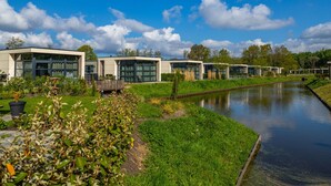 A modern building complex with large windows and a canal in the foreground. - Modern Holiday Home Near the Golf Course (Velsen-Zuid)