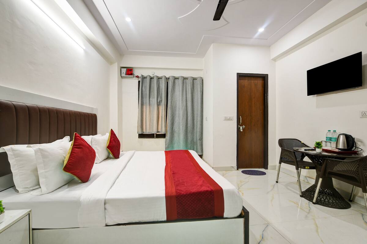 A hotel room with a bed, a desk, a chair, a television, and a door.