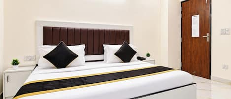 A modern hotel room with a large bed, a wooden door, and a small bedside table with a plant.