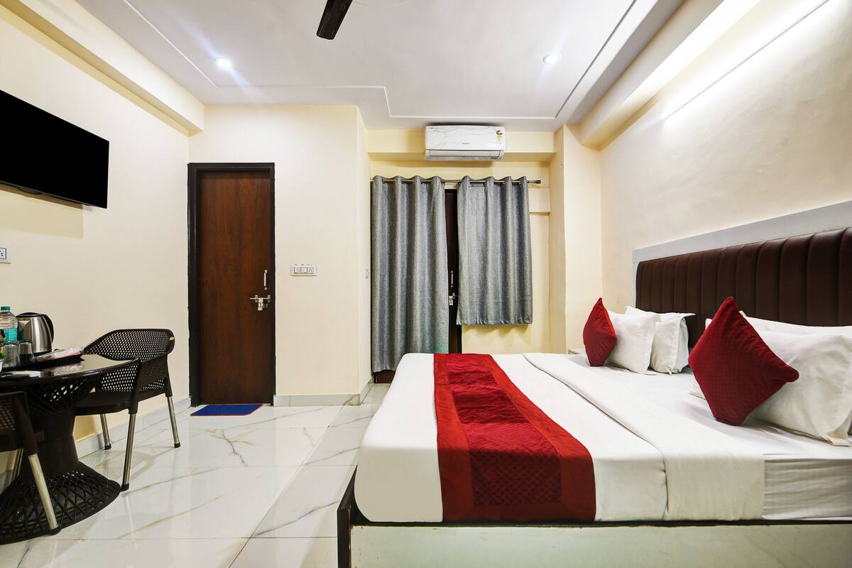 A hotel room with a bed, a desk, a chair, a television, and an air conditioning unit.