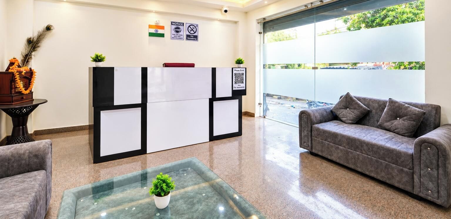 A reception area with a sofa, a glass coffee table with a plant, a notice board, and a view of the outside.