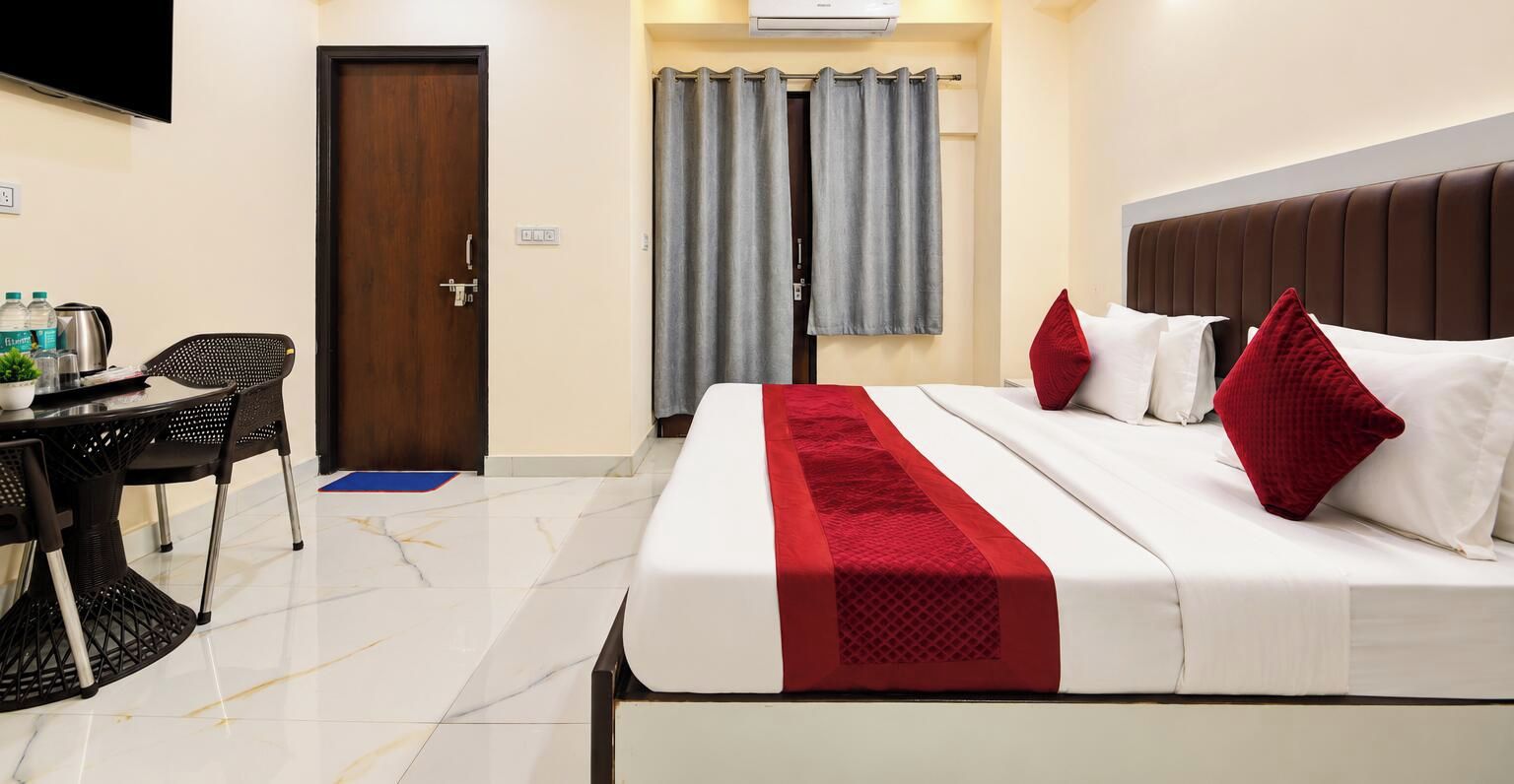 A hotel room with a bed, a desk with chairs, a television, and a window with curtains.