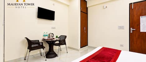 A hotel room with a bed, a TV, a table with chairs, and a red runner.