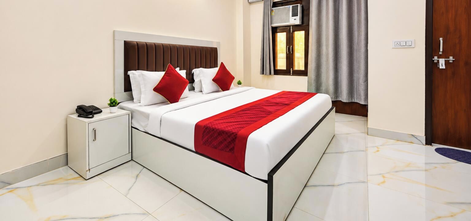 A hotel room with a bed, bedside table, and an air conditioning unit.
