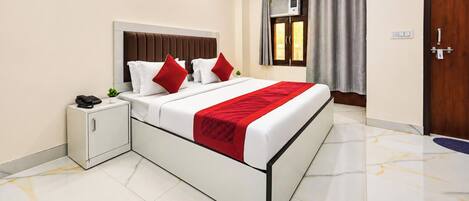 A hotel room with a bed, bedside table, and an air conditioning unit.