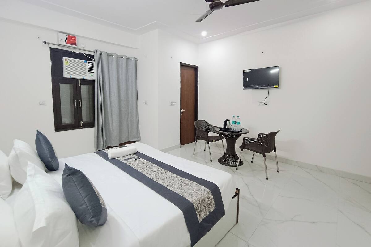 A hotel room with a bed, a ceiling fan, a TV, and a small table with chairs.