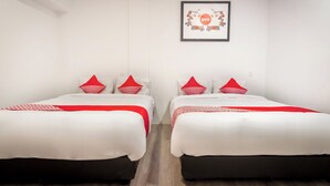 Habitación de hotel con dos camas, cada una con ropa blanca y detalles rojos, un cuadro en la pared y suelo de madera.