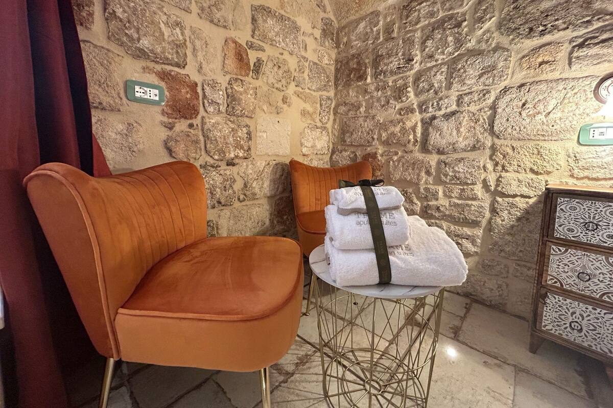 A corner room with a stone wall, a pair of orange chairs, a small table with towels, and a decorative cabinet.