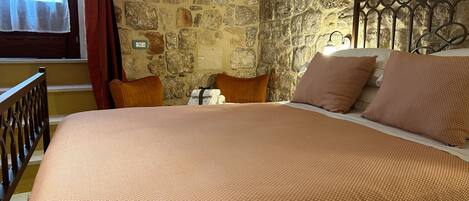 A bedroom with a stone wall, a bed with a brown blanket, two pillows, and a metal headboard.