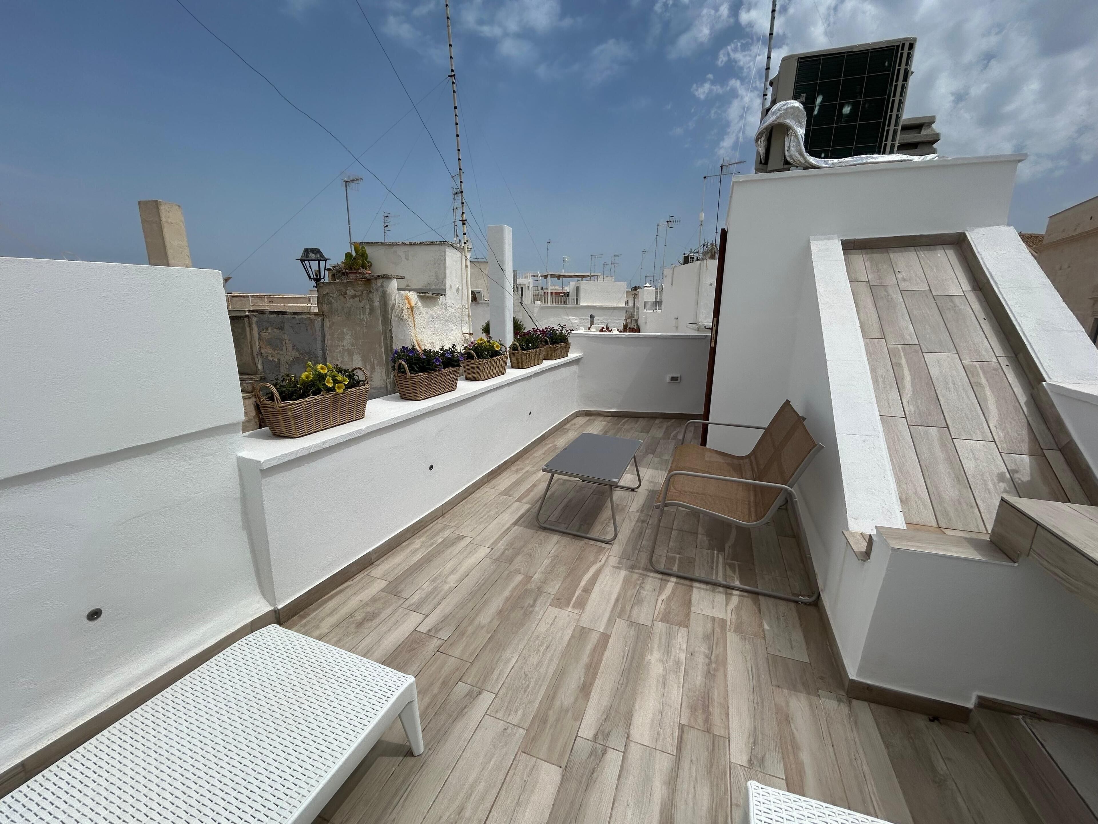 A rooftop terrace with a white bench, a small table, and potted plants.