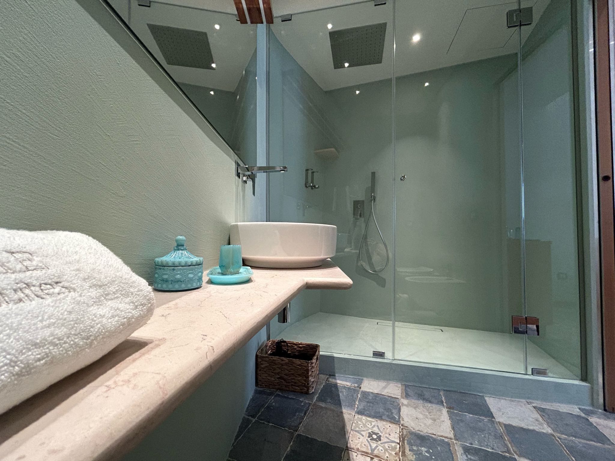 A modern bathroom with a glass-enclosed shower, a sink, and a shelf with toiletries.