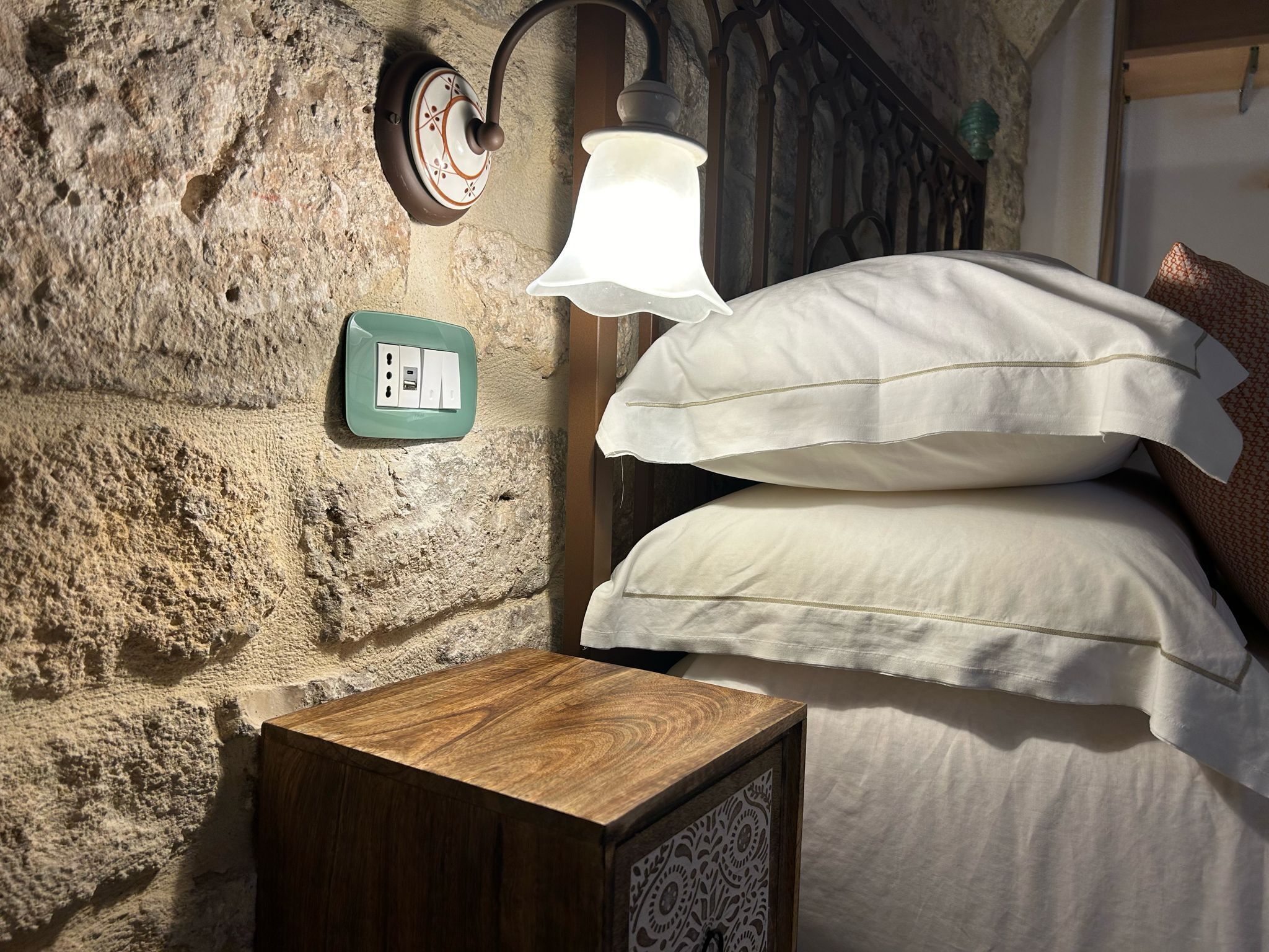 Una pared de piedra rústica con un aplique, un enchufe y una mesita de noche de madera con un cajón estampado.