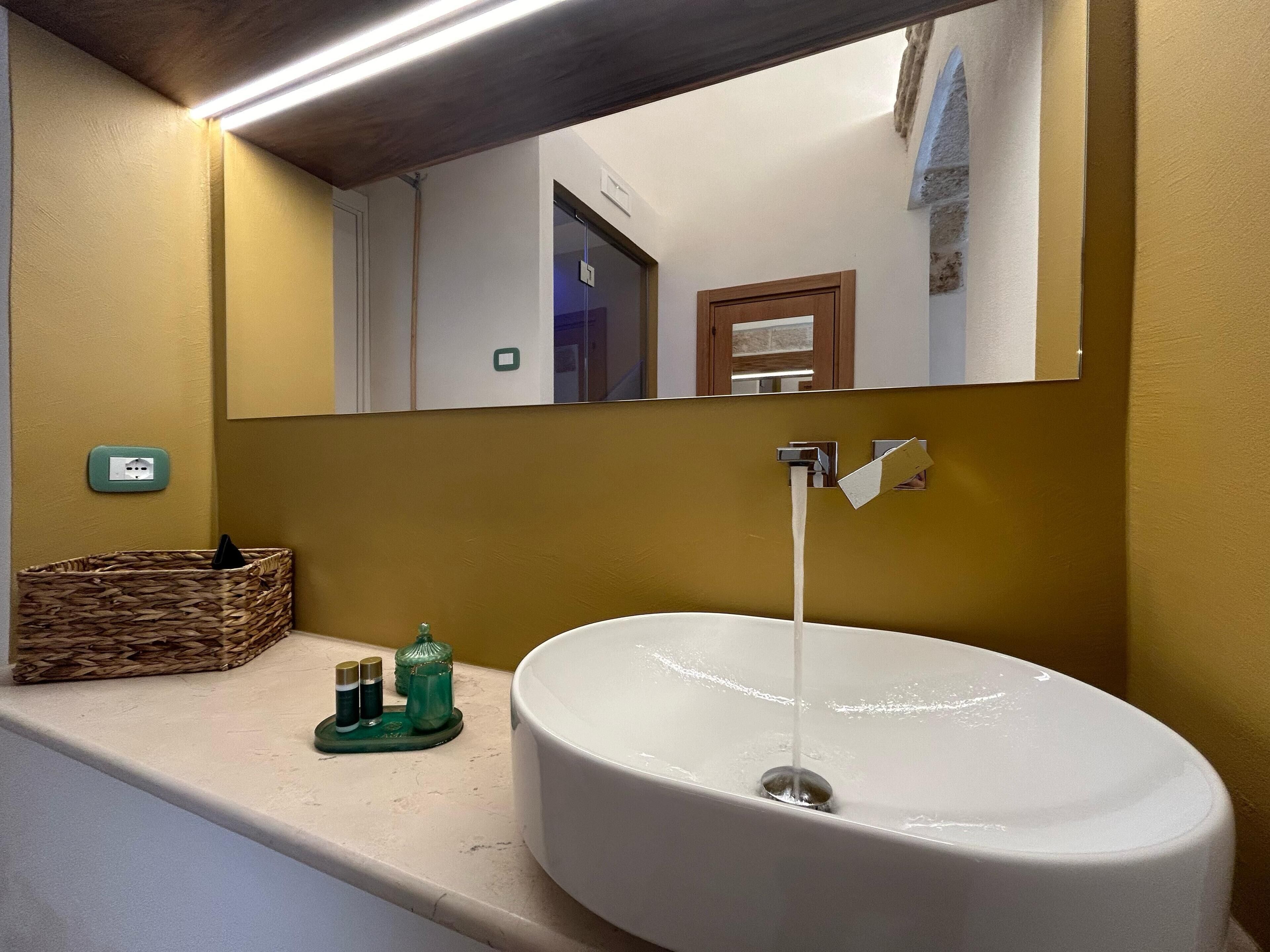 A bathroom with a white sink, a mirror, a wooden basket, and a green soap dispenser.