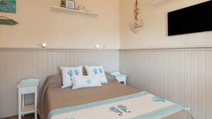A bedroom with a bed, nightstands, a shelf with decorative items, and a mounted TV. - Mishti Blu Studio al Mare by Wonderful Italy (Olbia)