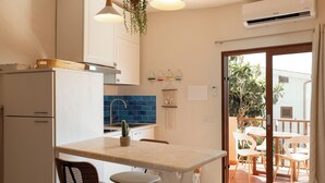 A kitchen with a central island, white cabinets, a blue backsplash, and a sliding glass door leading to an outdoor patio with chairs. - Mishti Blu Studio al Mare by Wonderful Italy (Olbia)