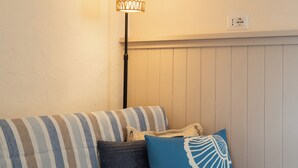 A striped sofa with two pillows, a floor lamp, and a wall with a painting and a small shelf. - Mishti Blu Studio al Mare by Wonderful Italy (Olbia)