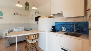 A compact kitchen with white cabinets, a blue-tiled backsplash, a coffee maker, and a hanging plant. - Mishti Blu Studio al Mare by Wonderful Italy (Olbia)