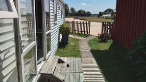 A wooden deck leading to a house with a sliding glass door and a potted plant. - Mobilhome en Presquîle Guerandaise Pour 4 Personnes (Saint-Molf)