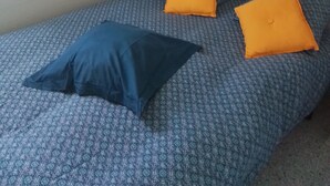 A single bed with patterned bedding and two pillows, one blue and one orange, in a room with a white wall and a framed picture. - Mobilhome en Presquîle Guerandaise Pour 4 Personnes (Saint-Molf)