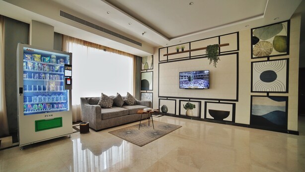 Uma sala de estar moderna com um sofá, uma mesa de centro, uma TV fixada na parede e uma máquina de vendas.