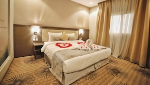 Quarto de hotel com uma cama grande, mesa de cabeceira e luminária na parede.