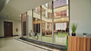 Um hall amplo com parede de vidro, balcão de recepção e vista para um pátio com mobiliário exterior.
