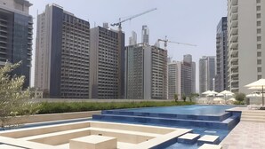 A modern urban setting with high-rise buildings, a swimming pool area with steps, and construction cranes in the background. - Near Dubai Mall 1BR  Reva Residence (Dubai)