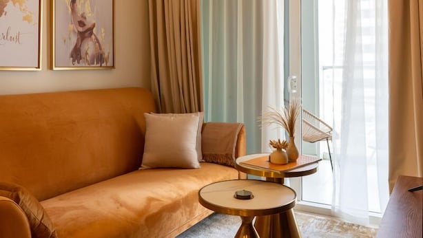 A modern living room with a sofa, a round coffee table, and a chair. There are two framed artworks on the wall and a window with curtains. - Near Dubai Mall 1BR  Reva Residence (Dubai)