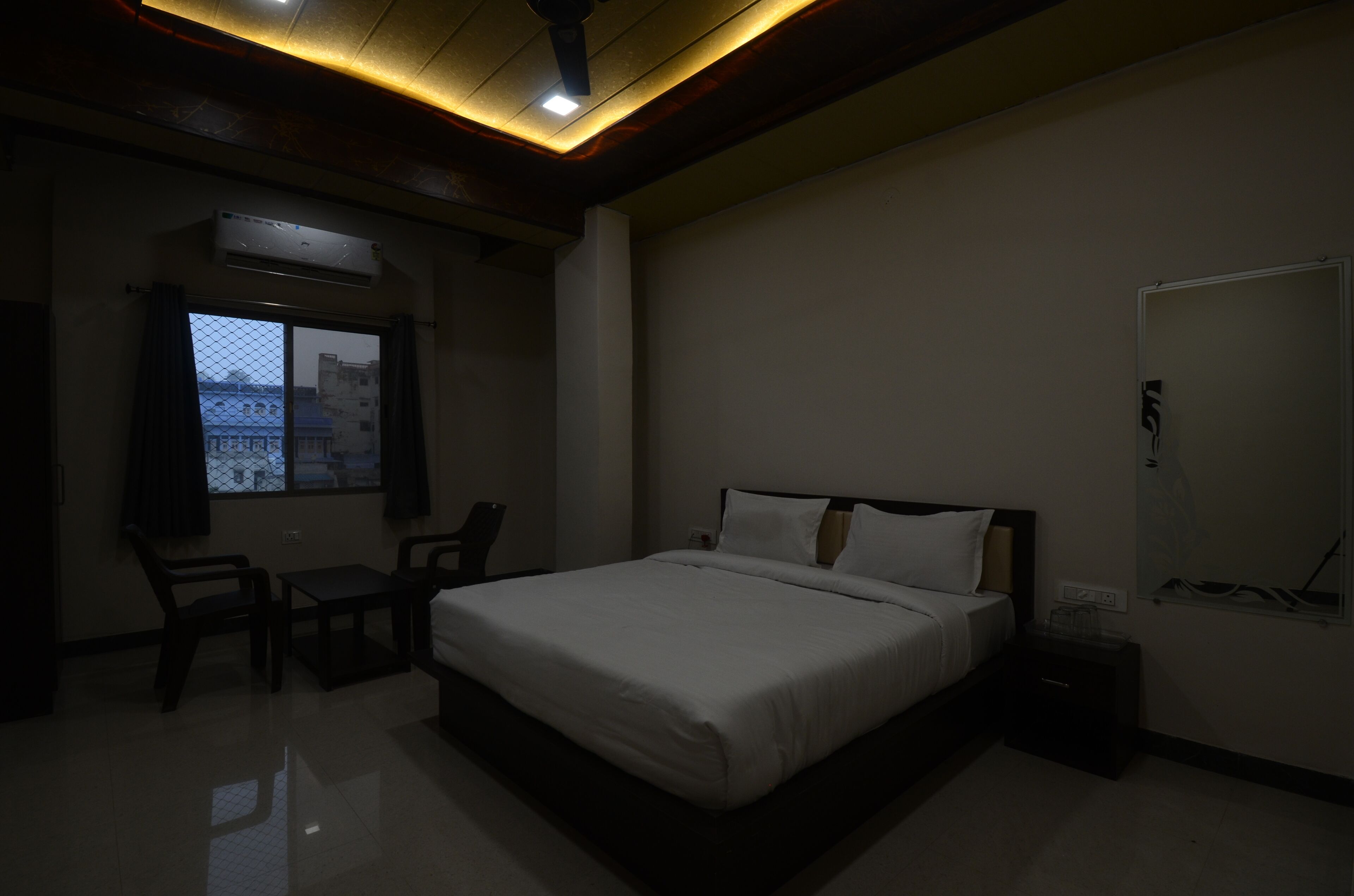 Une chambre à coucher avec un lit, un bureau et une chaise. Il y a une fenêtre avec des rideaux et un luminaire au plafond.