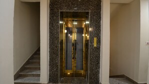 A modern elevator with a glass door and a marble surround, located at the entrance of a building with a tiled floor. - Hotel Shri Dhwaja Inn (Nathdwara)