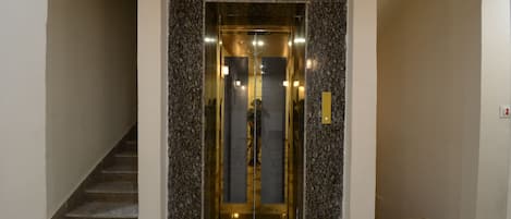 Un ascensor moderno con puerta de vidrio y detalles de mármol, situado en la entrada de un edificio con suelo de baldosas.