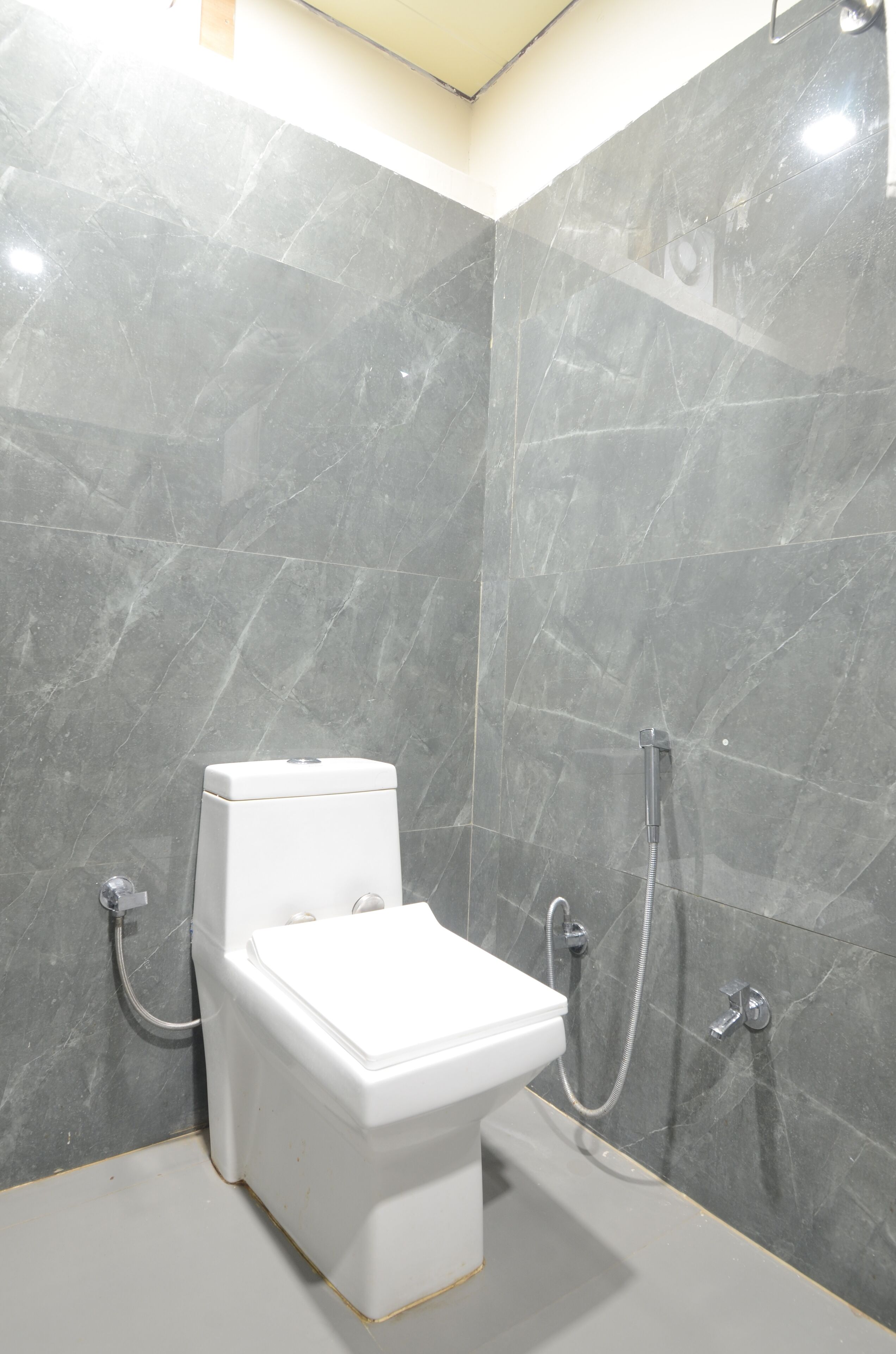 Et moderne badeværelse med et hvidt toilet, en bruser og en væg med marmorlignende finish.