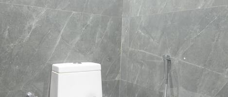Un baño moderno con inodoro blanco, ducha y pared con acabado similar al mármol.