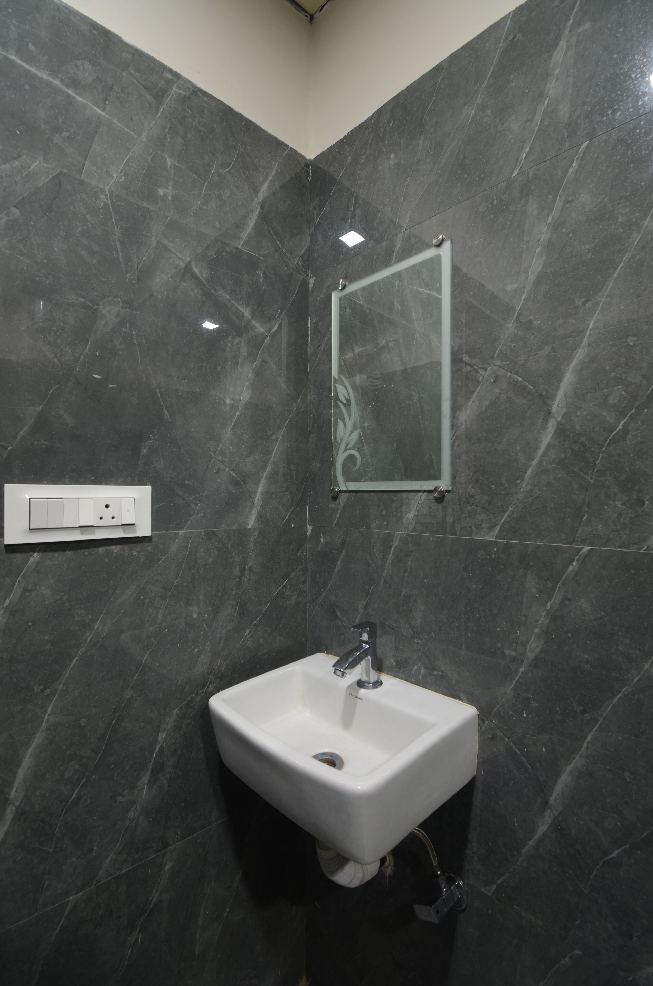 A bathroom with a white sink, dark marble walls, a mirror, and a light switch.