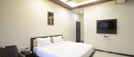 Habitación de hotel con cama, mesita de noche, silla, ventilador de techo, obra de arte, televisión y puerta.