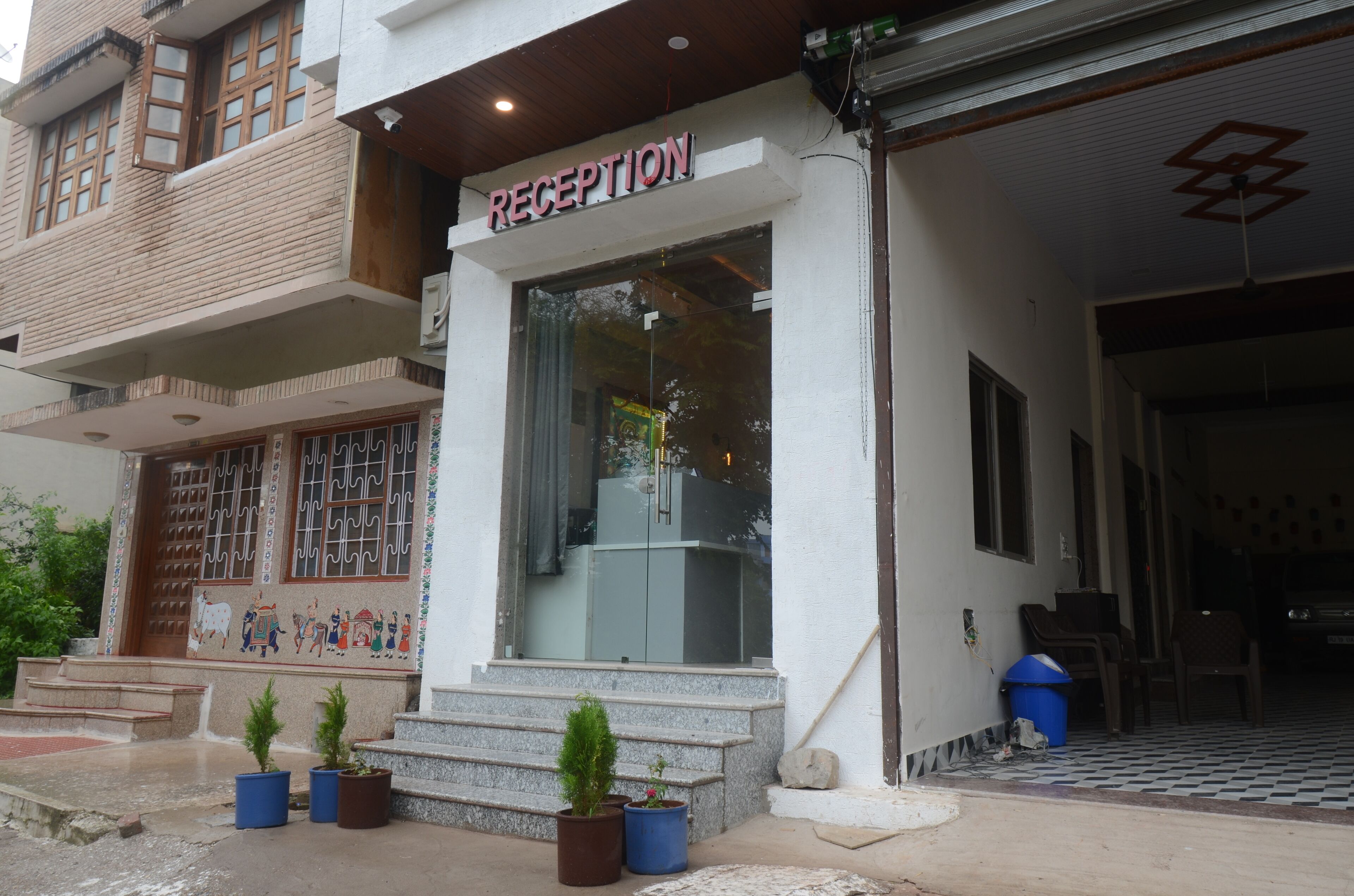 A reception area with a sign, steps leading up to the entrance, and potted plants.
