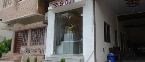 A reception area with a sign, steps leading up to the entrance, and potted plants.