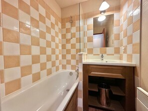 A bathroom with a checkered tile wall, a white bathtub, a wooden vanity with a sink, and a mirror. - 1-bedroom apartment, ski-in/ski-out, pool, up to 4 guests (Vars)