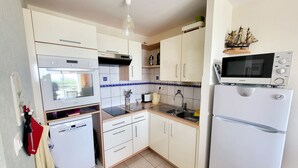 A compact kitchen with white cabinets, a built-in oven, a microwave, and a sink. - Seaview Apartment with Balcony, 2 Bedrooms, Parking, Close to Beaches & Shops (Les Sables-d'Olonne)
