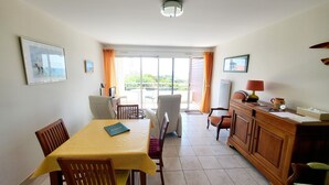 A dining area with a table, chairs, and a view through a glass door to an outdoor balcony. - Seaview Apartment with Balcony, 2 Bedrooms, Parking, Close to Beaches & Shops (Les Sables-d'Olonne)
