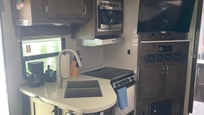 Cocina compacta para camper con microondas, estufa, lavabo y televisor de pantalla plana.