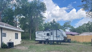 Una autocaravana estacionada en un patio trasero, con una casa y una valla de madera al fondo.