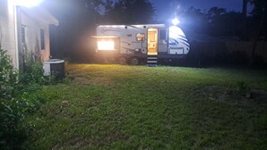 Una autocaravana estacionada en un patio trasero, con un interior bien iluminado y una puerta visible.