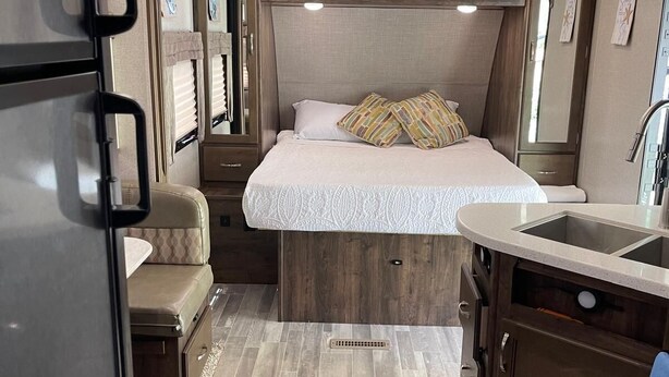 Interior compacto de autocaravana con cama, kitchenette y armarios de almacenamiento.