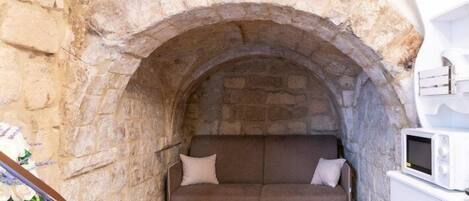A stone archway leading to a cozy seating area with a sofa and a microwave on a white cabinet.