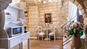 Ein gemütliches Zimmer mit Steinwand, einem weißen Schreibtisch mit Mikrowelle, zwei Stühlen, einem kleinen Tisch mit Blumenvase und einer Chandelier.
